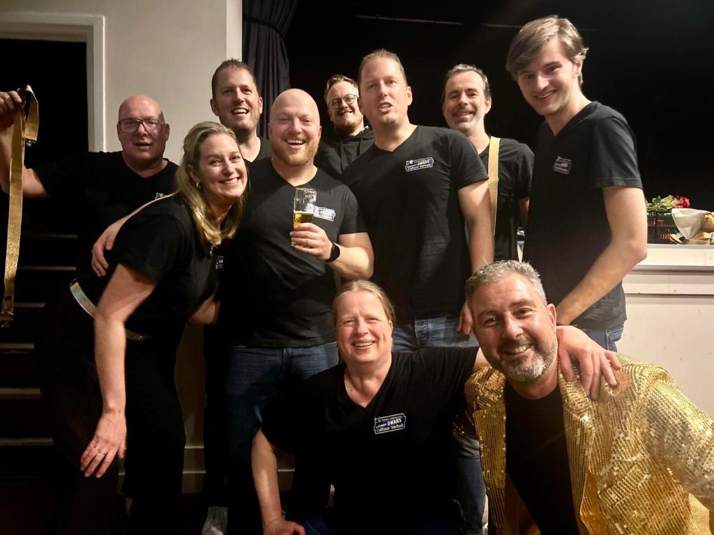 De spelers van theatersportgroep Dwars in zwarte Dwars-shirts, lachend bij elkaar na een voorstelling.