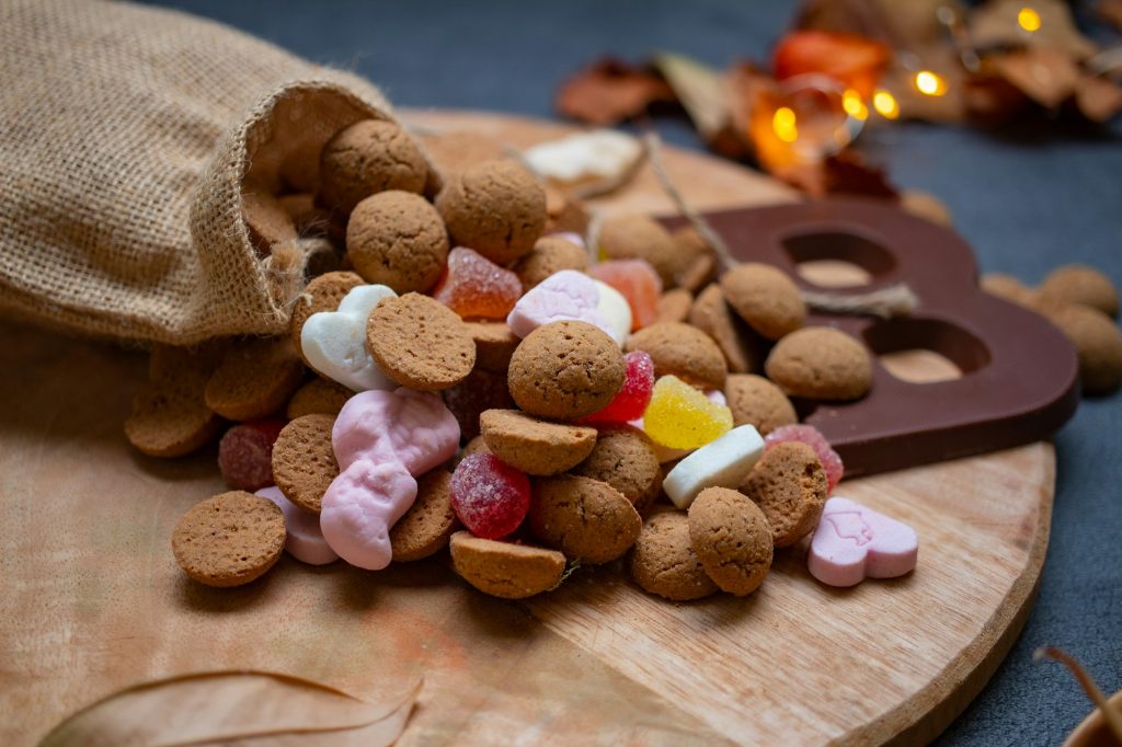 Een jute zak met kruidnoten, schuimpjes en een chocoladeletter op een houten plank.